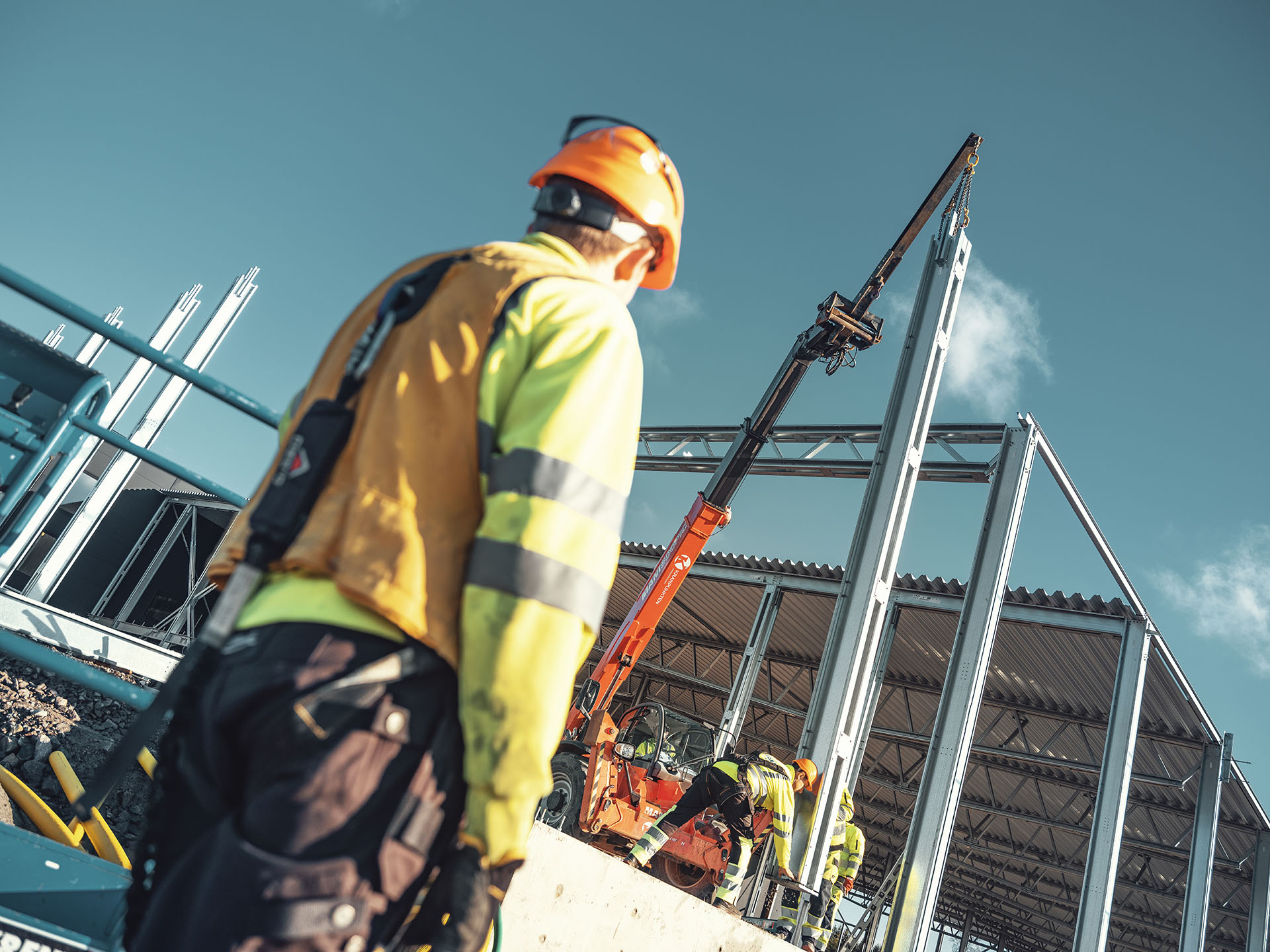 Byggarbetare med skyddshjälm, varselkläder och fallskydd på byggarbetsplats.
