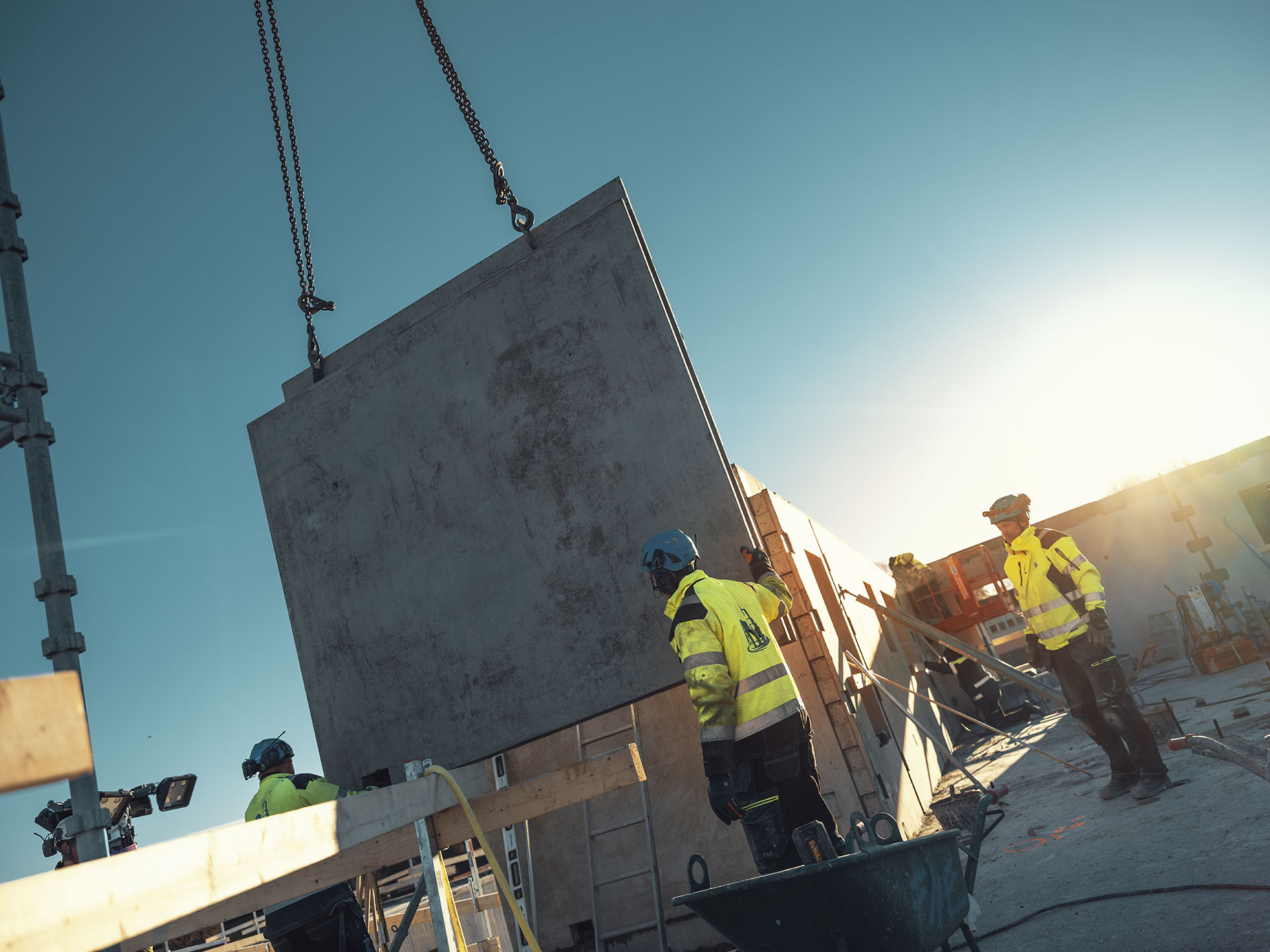 Personer med skyddshjälm, hörselkåpor och varselkläder på byggarbetsplats.