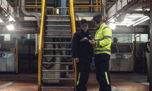 Personer med varselkläder och hörselkåpor pratar om personlig skyddsutrustning.