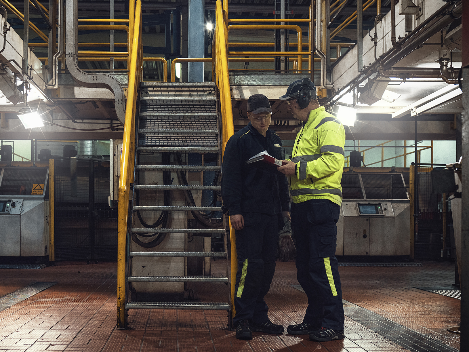 Personer med varselkläder och hörselkåpor pratar om personlig skyddsutrustning.