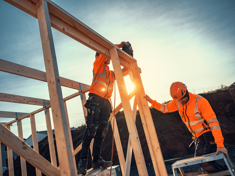 Byggarbetare i skyddshjälm och varselkläder bygger stommar för hus.