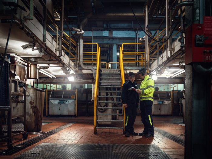 Personer med varselkläder och hörselkåpor pratar om personlig skyddsutrustning.