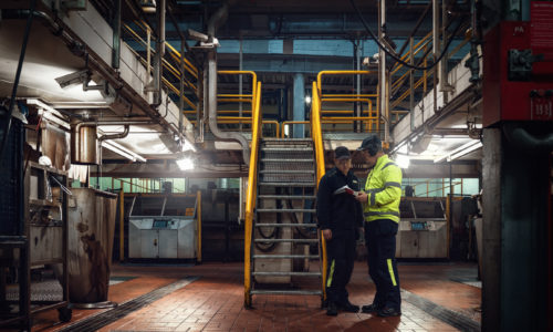 Personer med varselkläder och hörselkåpor pratar om personlig skyddsutrustning.