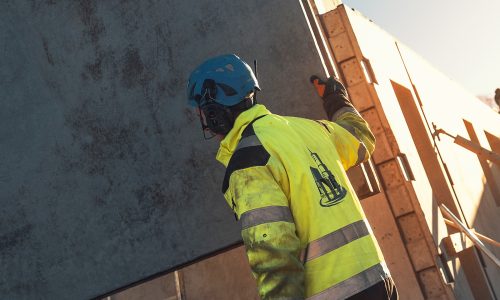 Bild på byggarbetare som håller i ett betongblock. Han har handskar på sig.