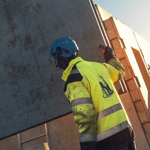 Bild på byggarbetare som håller i ett betongblock. Han har handskar på sig.