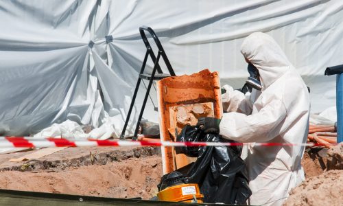 Person iklädd korttidsoverall och andningsskydd arbetar med sanering av asbest.