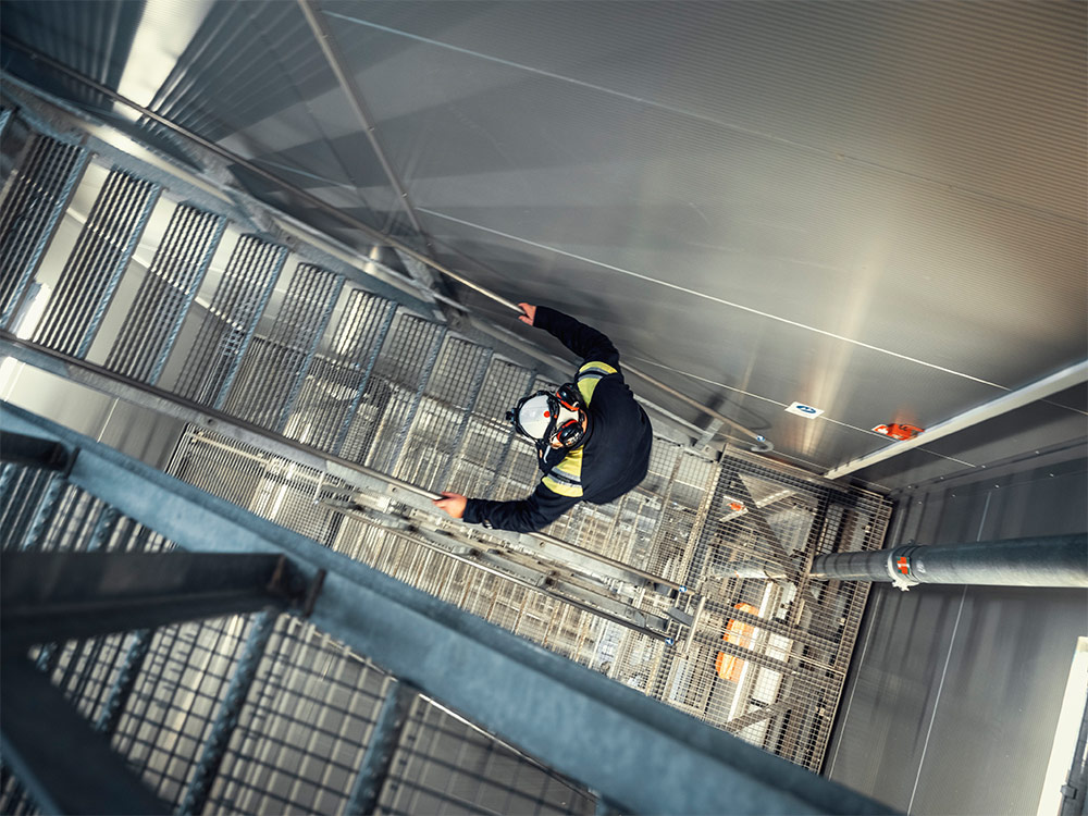 Man som klättrar i trappa på hög höjd. Industriarbetaren bär skyddshjälm.